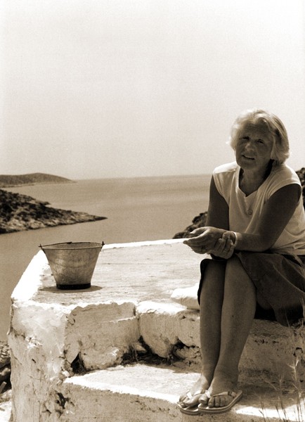 Katherine Allfrey in Griechenland um 1980. Allfrey sitzt auf einem hellen Stein, im Hintergrund sieht man eine weite Meerlandschaft.